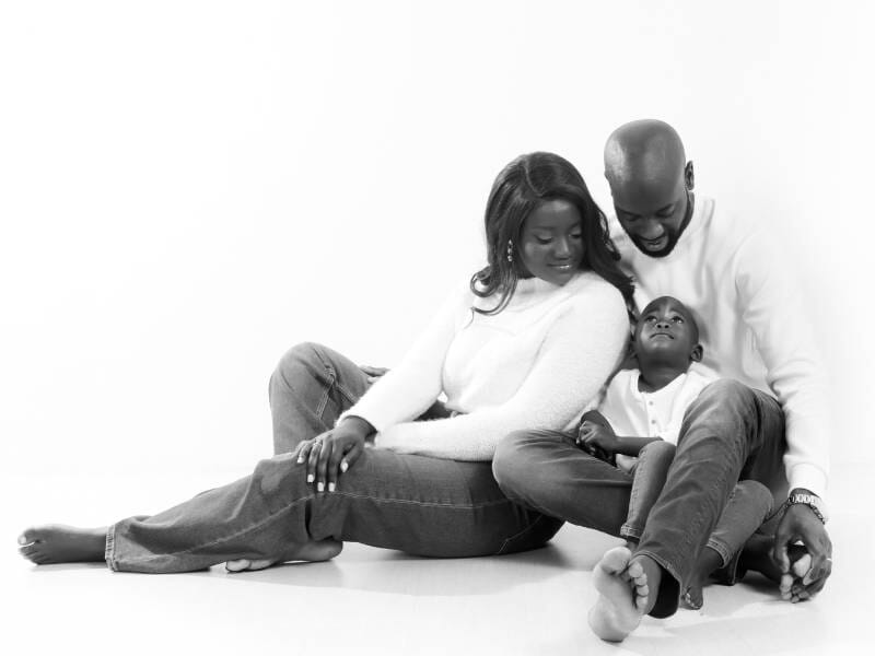 Un couple et son enfant sont assis au sol et prennent la pose.