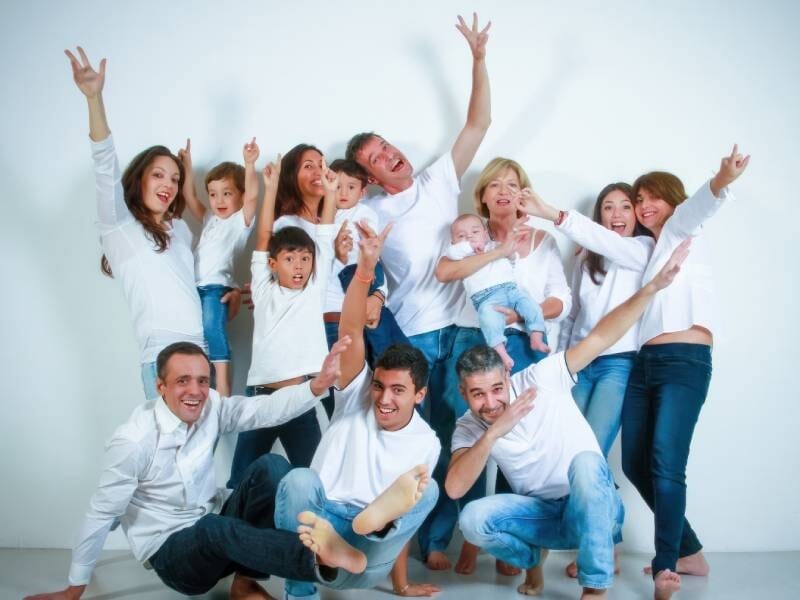 Une famille nombreuse, dont tous les membres sont vêtus d'un haut blanc et d'un jean, prend une pose festive.