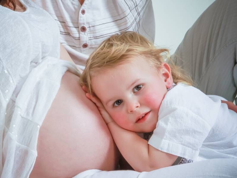 Un jeune enfant pose son oreille contre le ventre de sa maman enceinte.