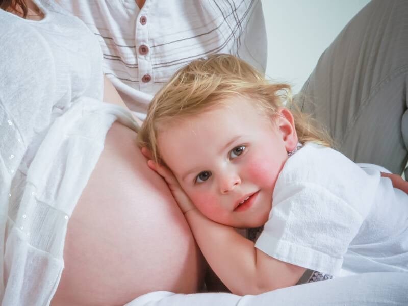 Un jeune enfant pose son oreille contre le ventre de sa maman enceinte.