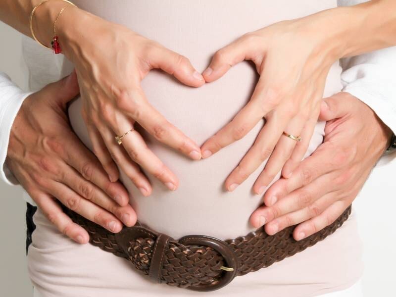 Deux paires de mains posées sur le ventre d'une femme enceinte, celles de la femme forment un coeur.