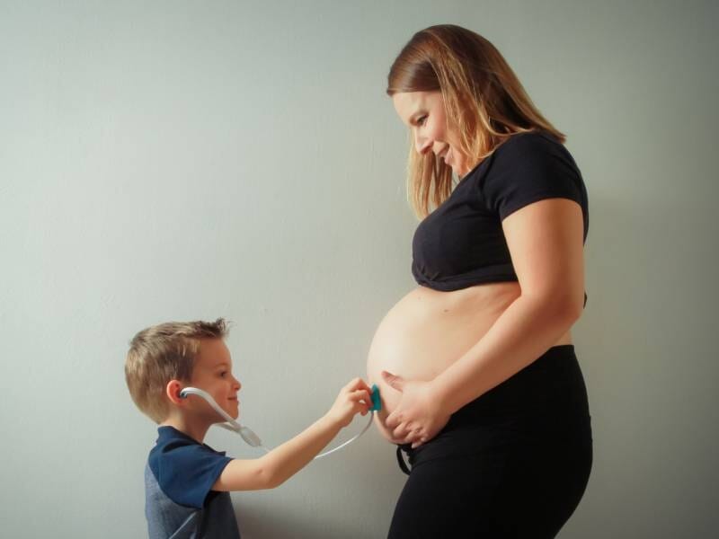 Un enfant avec un faux stéthoscope écoute le ventre de sa maman enceinte.