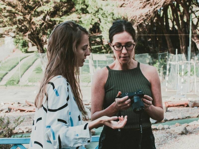 Une femme en train de montrer quelque chose sur son appareil photo à une autre femme.