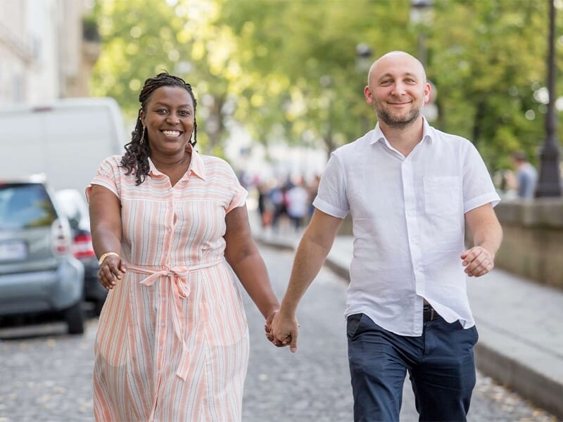 Couple se tenant la main en marchant dans une rue pavée, visiblement joyeux, vêtements d’été.