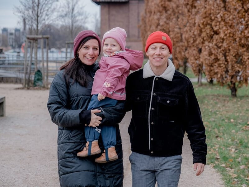 Couple habillé chaudement tenant une fillette en manteau rose, tous souriants lors d’une promenade hivernale.