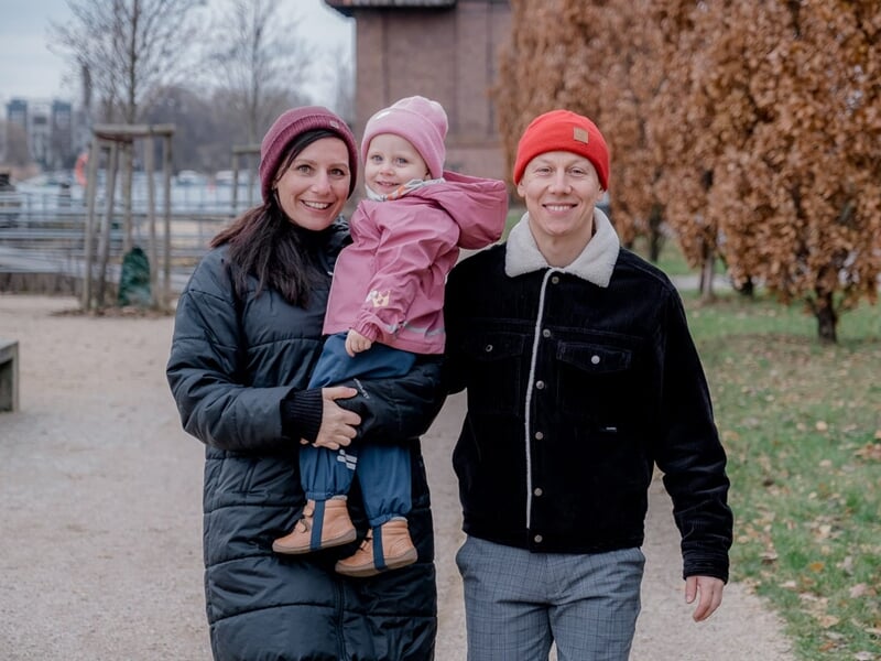 Couple habillé chaudement tenant une fillette en manteau rose, tous souriants lors d’une promenade hivernale.