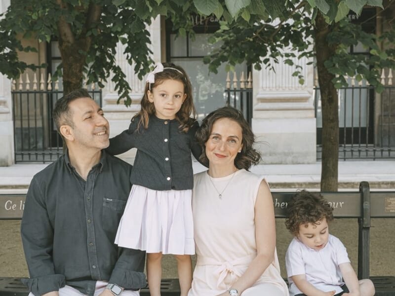 Famille assise sur un banc, deux parents et deux enfants, la fille debout entre eux, le garçon regarde vers le sol.