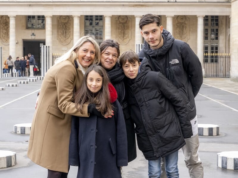 Groupe de cinq personnes posant devant les colonnes du Palais-Royal, tous vêtus de manteaux d’hiver.