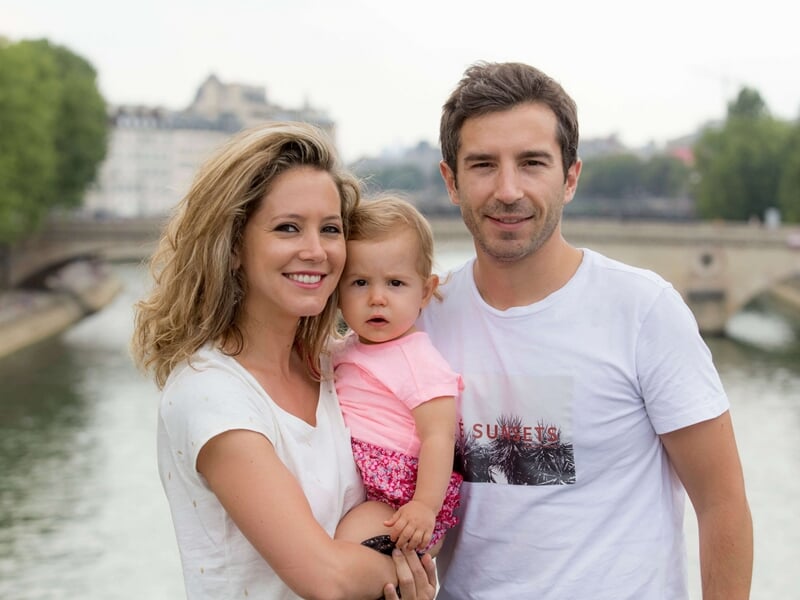 Couple tenant une fillette en bas âge, tous souriants, posant sur un pont au bord de la Seine.