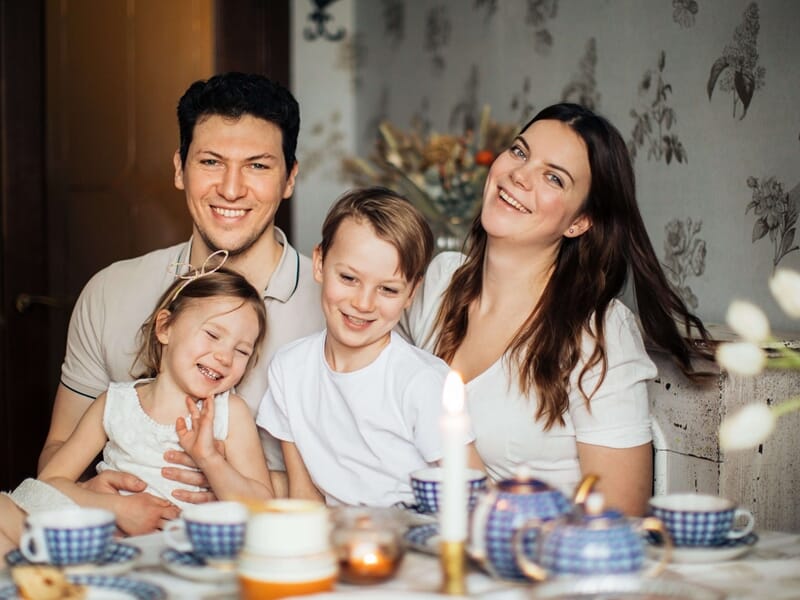 Famille de quatre réunie autour d’une table décorée, deux enfants rient, ambiance chaleureuse et conviviale.