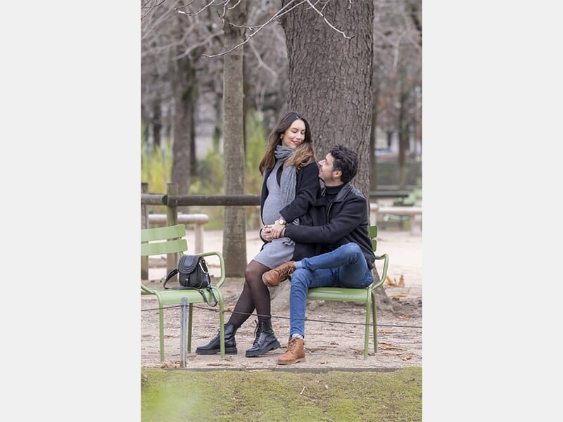 Couple assis sur des chaises dans un parc, l’homme enlace la femme enceinte qui sourit en le regardant.