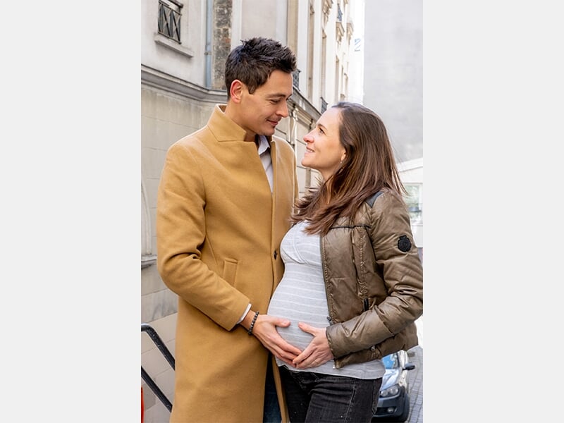 Couple se regardant tendrement dans la rue, les mains posées sur le ventre arrondi de la femme enceinte.
