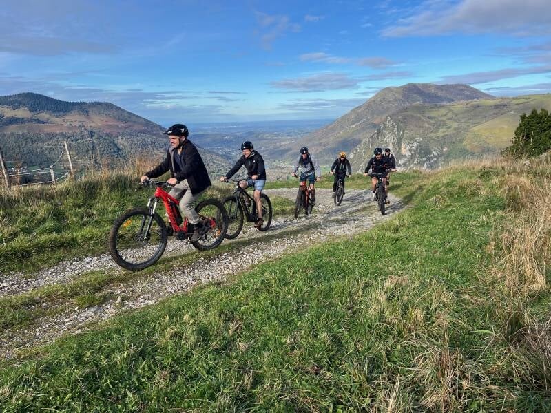 Cinq cyclistes parcourent une piste herbeuse au milieu des montagnes.