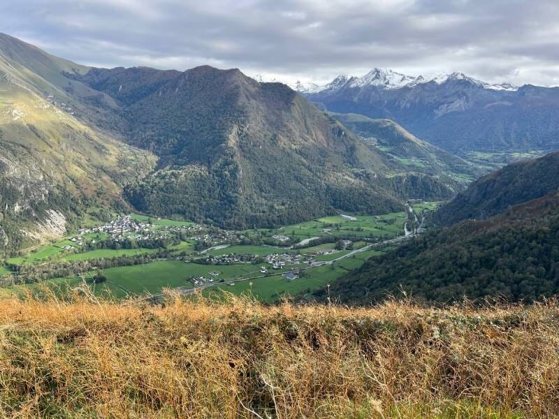 Vue sur la vallée verdoyante et les montagnes enneigées en toile de fond.