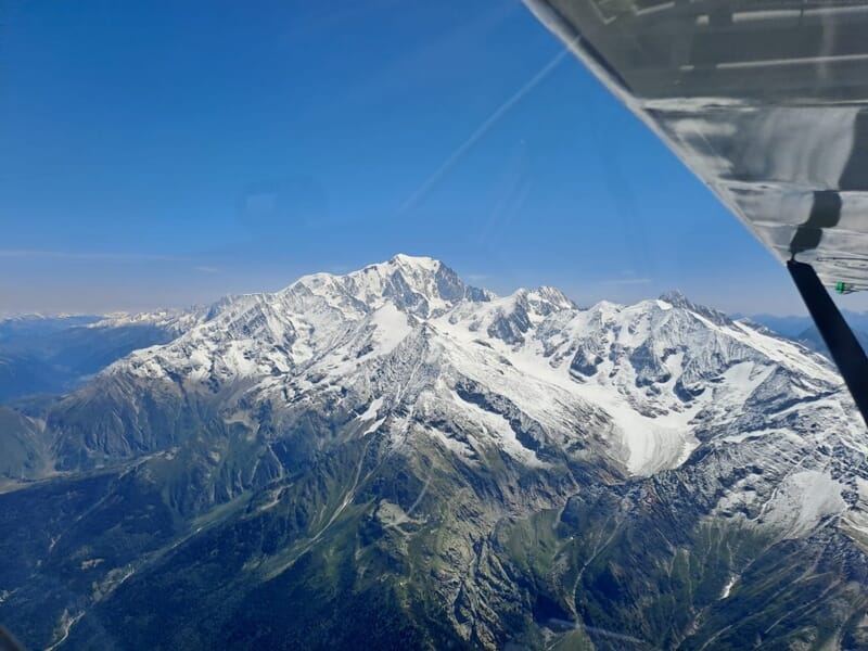 Vue aérienne du Mont Blanc depuis un petit avion, avec l’aile visible sur la droite de l’image, sous un ciel bleu dégagé.