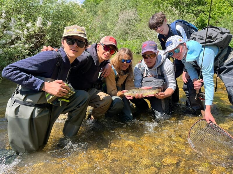 Jeunes pêcheurs en cuissardes posant dans une rivière peu profonde avec une truite brune fraîchement pêchée.