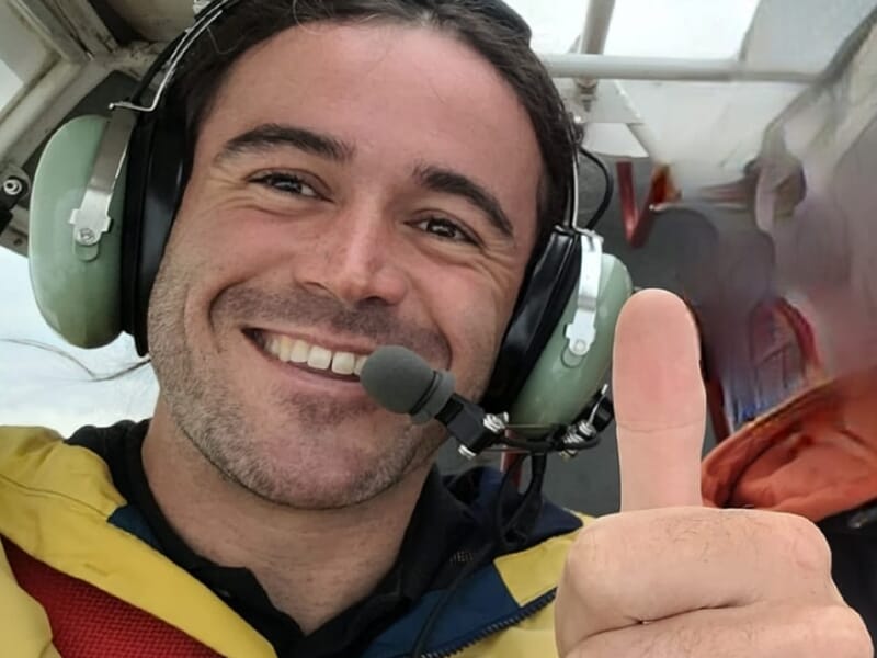 Portrait d’un pilote souriant à bord d’un ULM, casque sur les oreilles et pouce levé vers la caméra