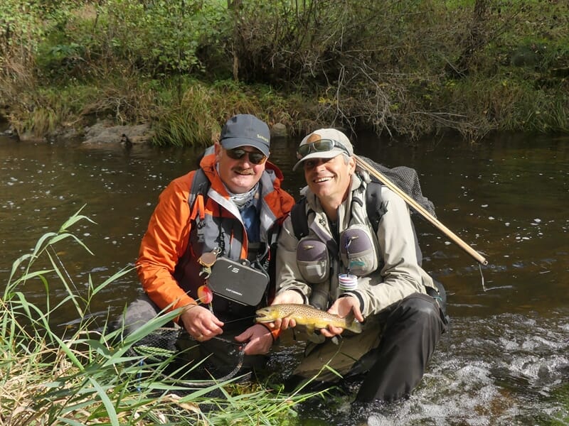 Deux pêcheurs à la mouche posant ensemble avec une truite capturée dans une rivière forestière