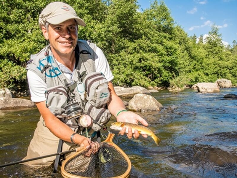 Pêcheur expérimenté en rivière tenant une truite avec une épuisette et un gilet de pêche complet