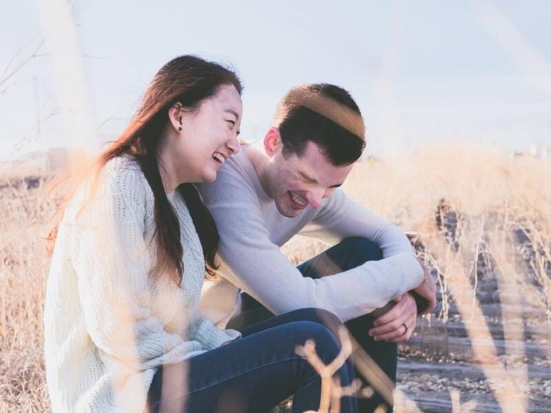 Un jeune couple assis dans un champ ensoleillé, riant et profitant d'un moment de détente en plein air.