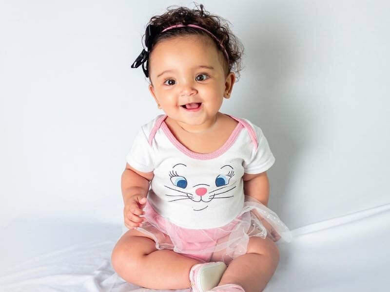 Bébé assis souriant, habillé d'un body blanc avec un dessin de chat et une jupe rose en tulle, pendant un shooting photo à Orléans.