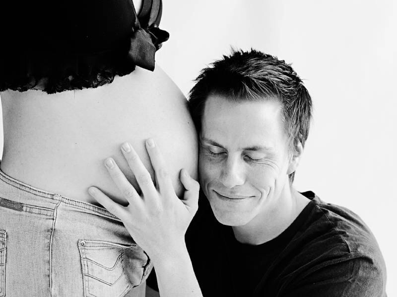Un homme pose sa tête contre le ventre arrondi d'une femme enceinte, exprimant tendresse et bonheur.