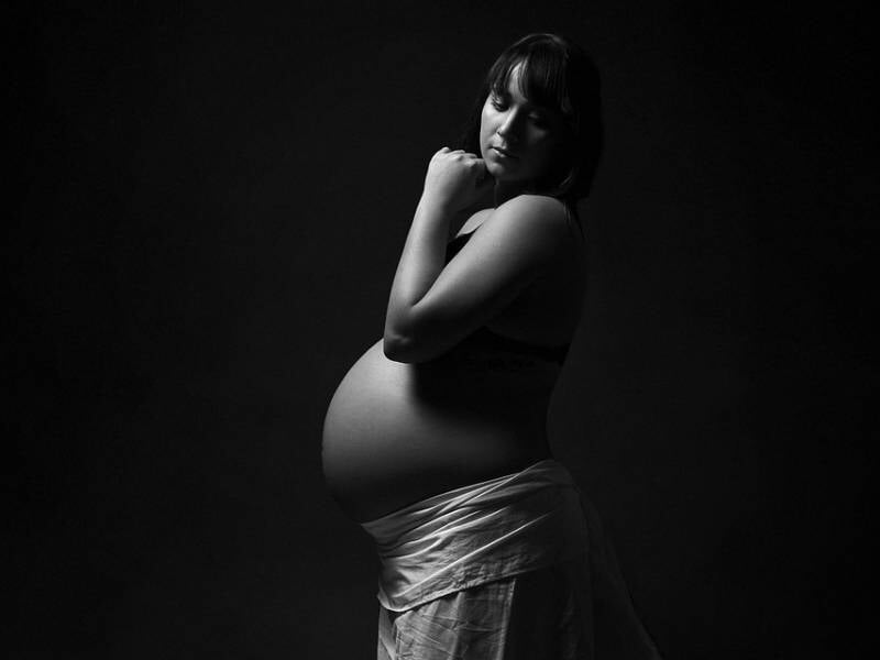 Une femme enceinte en profil, drapée d'un tissu clair, pose dans une ambiance sombre et intime, lors d'un shooting photo à Orléans.