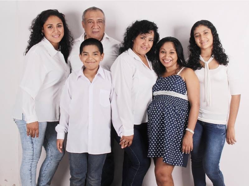 Portrait en studio d'une famille souriante composée de six personnes habillées en blanc et bleu, posant ensemble.