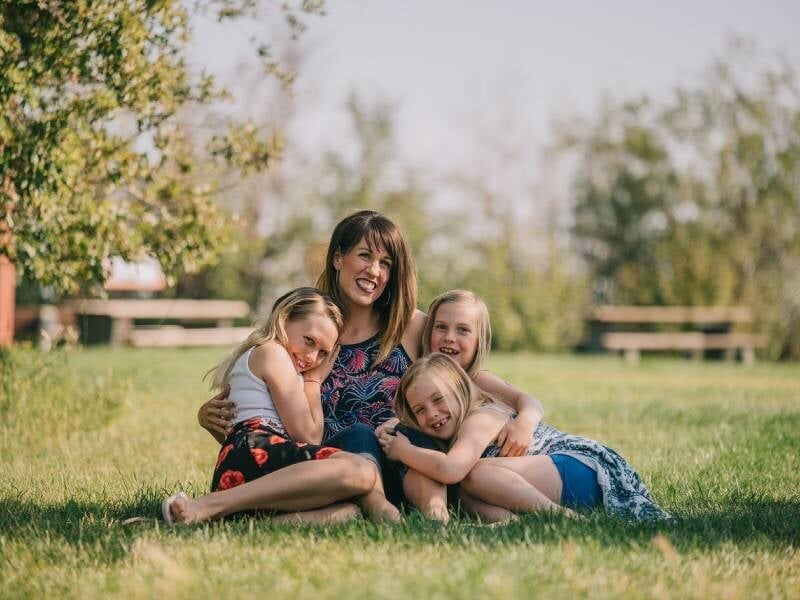 Une femme et trois enfants assis sur l'herbe dans un parc, souriants et profitant d'une journée ensoleillée, lors d'un shooting photot à Orléans.