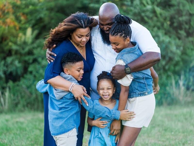 Une famille de cinq personnes s'enlaçant joyeusement dans un cadre naturel verdoyant, exprimant bonheur et amour.