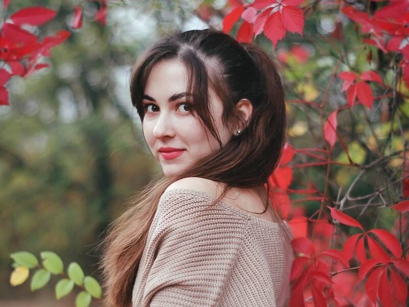 Jeune femme aux cheveux bruns attachés, regardant par-dessus son épaule, entourée de feuillage rouge et vert lors d'un shooting photo à Orléans.
