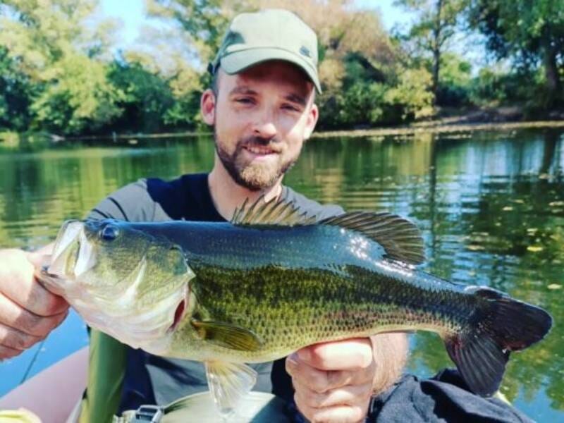 Un jeune homme présente un poisson blanc, vert et noir, un black bass.