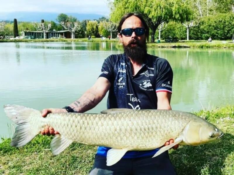 Un homme prend la pose avec une énorme carpe au bord de l'eau.