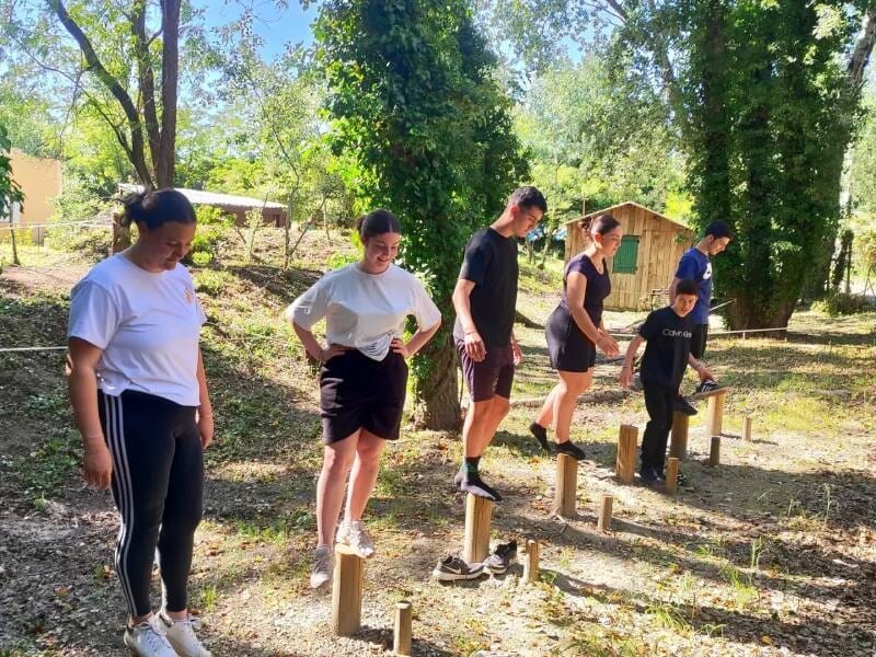 Six personnes tentent de garder l'équilibre sur des petits poteaux, au milieu de la forêt.