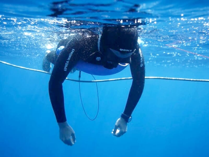 Plongeur en apnée flottant en surface, équipé d’une combinaison noire et d’une bouée de sécurité.