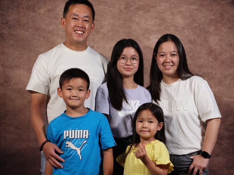 Portrait de famille de cinq personnes devant un fond marron, tous souriants.