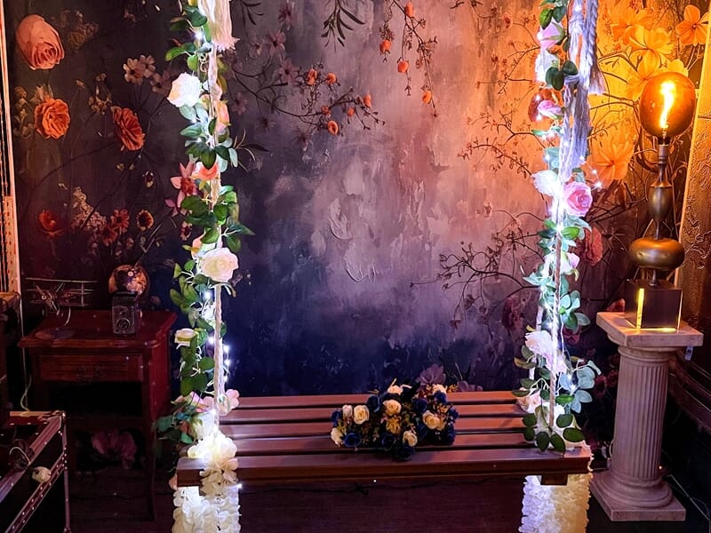 Balançoire en bois décorée de fleurs et de guirlandes lumineuses, fond floral romantique.