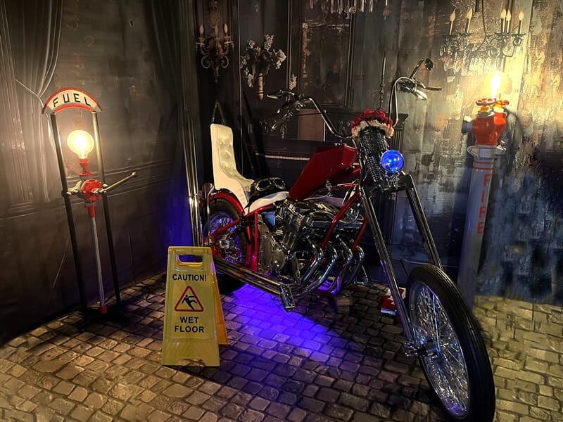 Moto custom rouge et chrome dans un décor rétro avec pompes à essence et éclairages chauds.