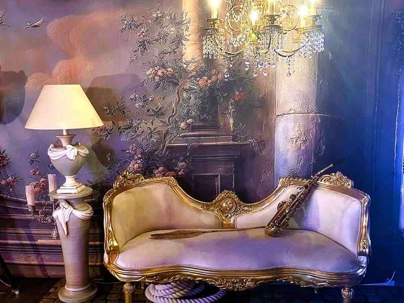 Canapé ancien doré avec saxophone, lampadaire et lustre en cristal, ambiance élégante et classique.
