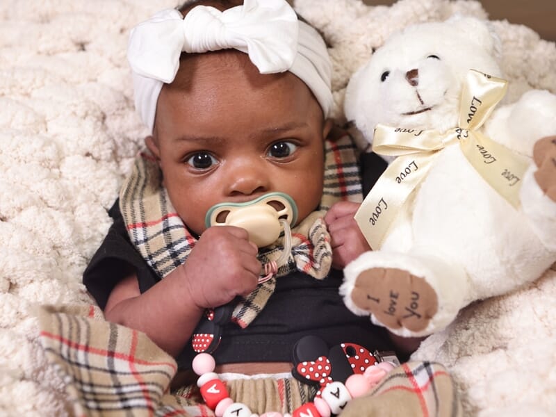 Bébé avec un bandeau blanc et tétine, tenant un ours en peluche blanc.