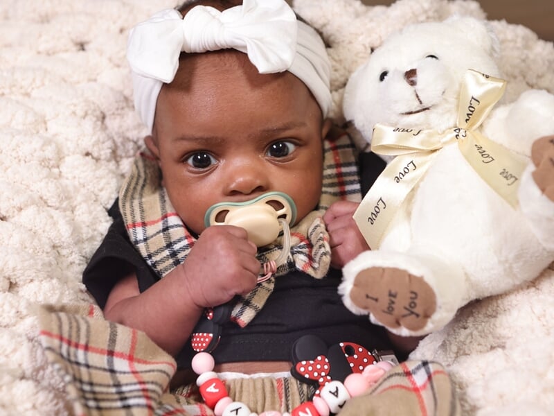 Bébé avec un bandeau blanc et tétine, tenant un ours en peluche blanc.