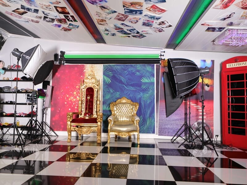 Studio photo aménagé avec fauteuils dorés style trône, éclairages professionnels, décor coloré et cabine téléphonique rouge