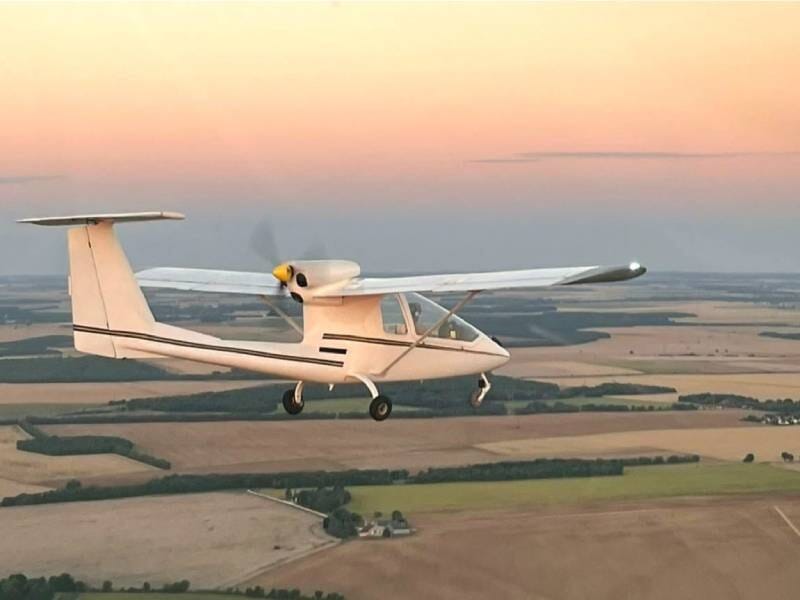 Vue sur le côté d'un avion ULM Sky Arrow 500 FT en vol au-dessus des champs. La lumière évoque un coucher de soleil.