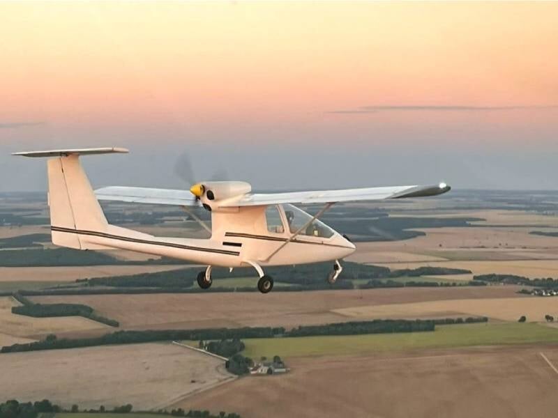 Vue sur le côté d'un avion ULM Sky Arrow 500 FT en vol au-dessus des champs. La lumière évoque un coucher de soleil.