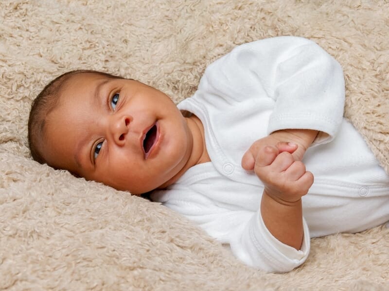 Bébé allongé sur le dos, habillé en blanc, allongeant ses bras, sur une couverture douce.