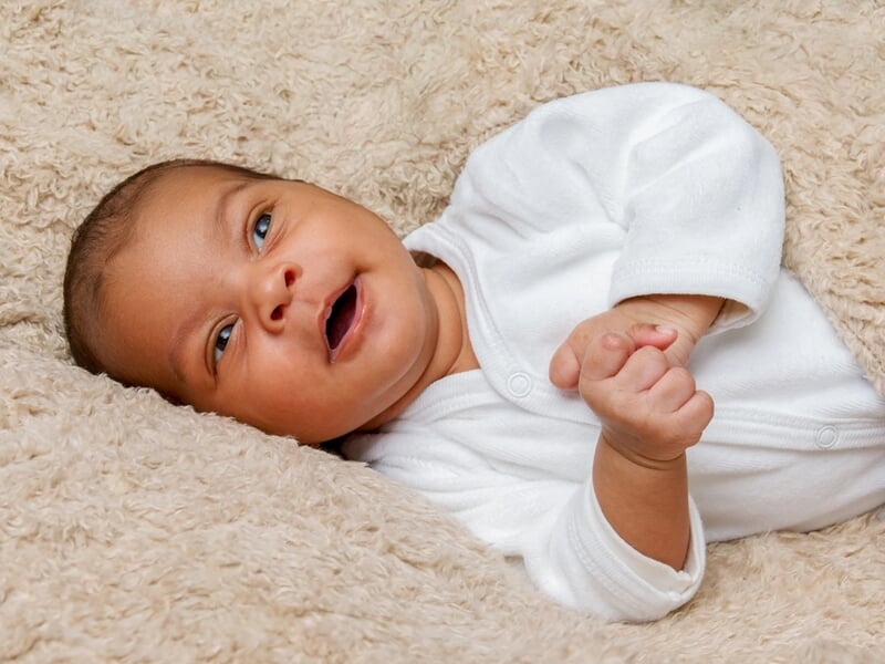 Bébé allongé sur le dos, habillé en blanc, allongeant ses bras, sur une couverture douce.