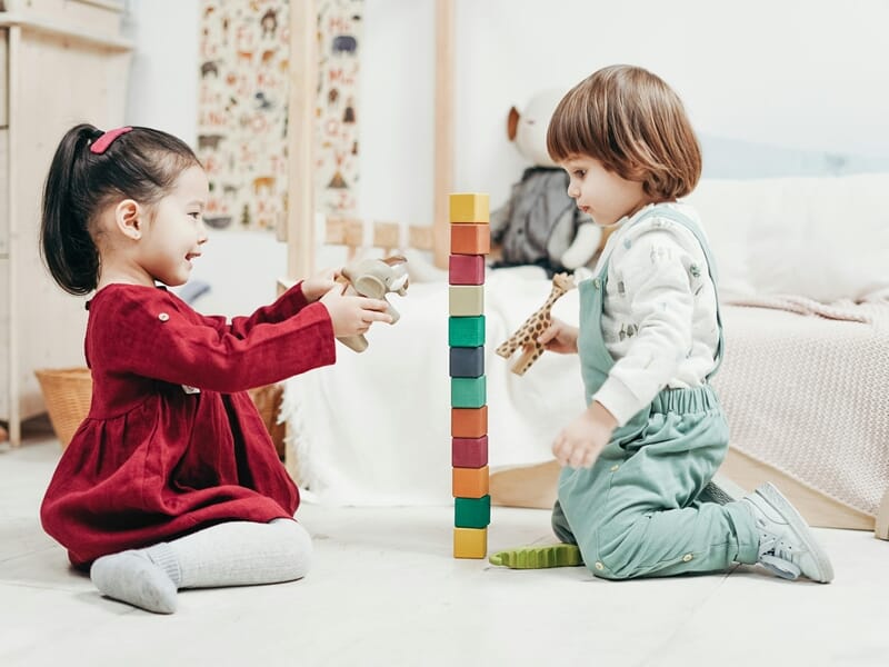 Deux enfants assis face à face construisant une tour avec des blocs colorés en bois.