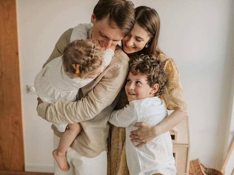 Parents serrant tendrement leurs deux jeunes enfants dans leurs bras à la maison.