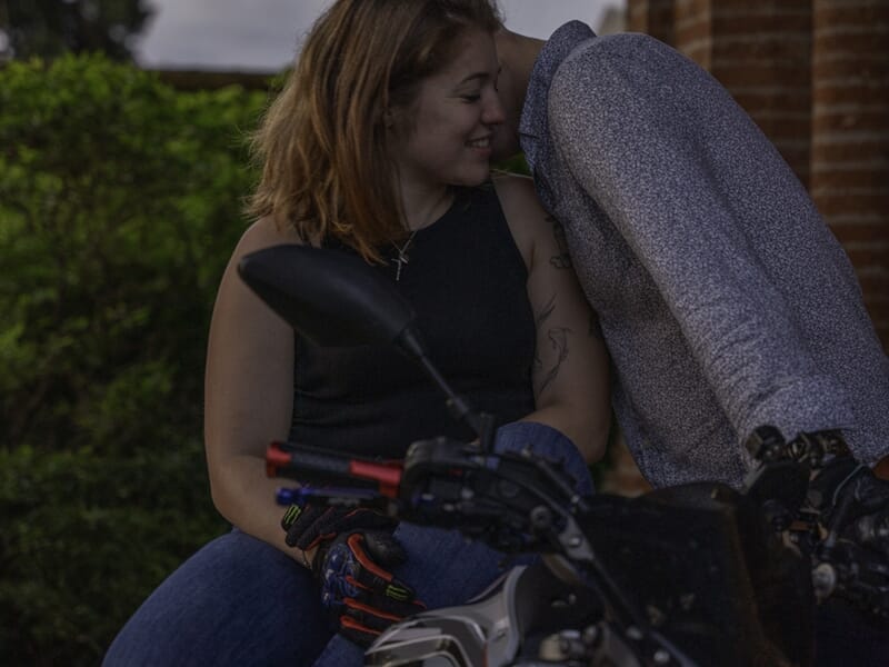 Couple assis sur une moto, partageant un moment tendre et complice.