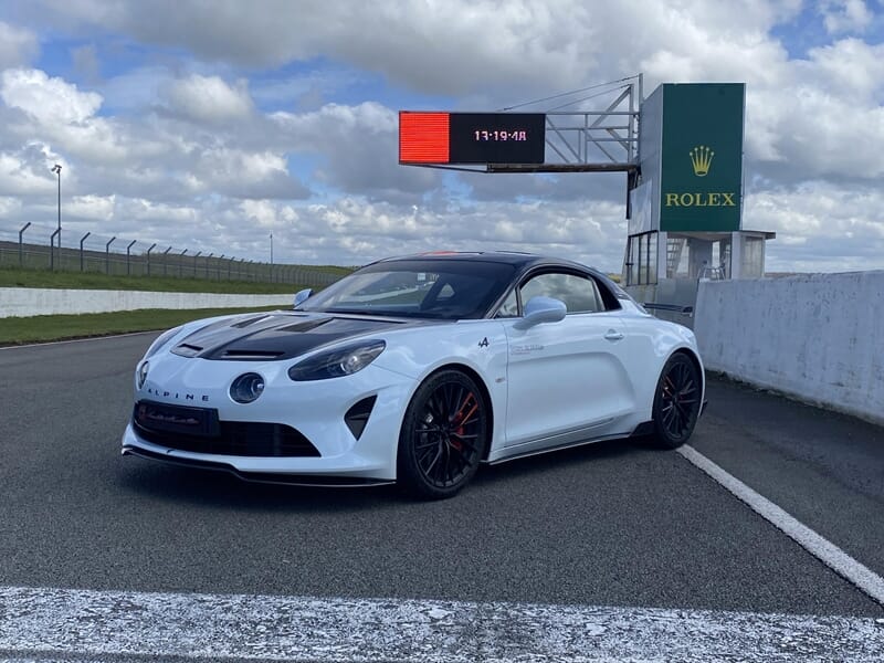 Voiture Alpine A110R blanche et noire garée sur piste devant panneau Rolex d’un circuit automobile